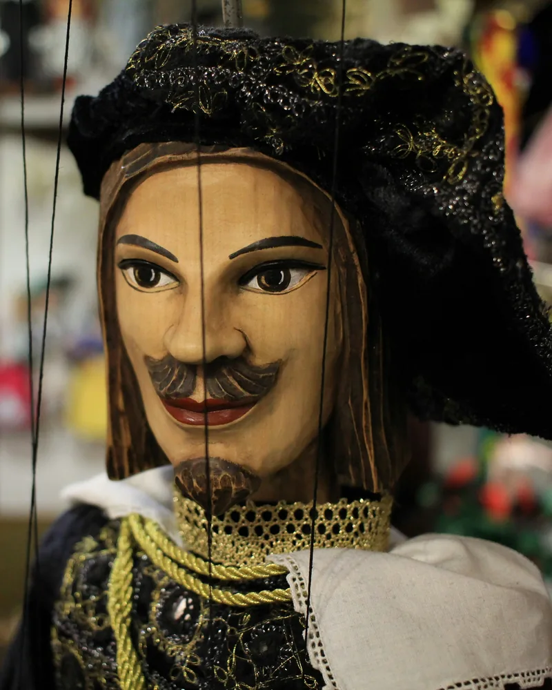 Dřevěná marioneta v historickém kostýmu zavěšená na nitích v loutkářské dílně